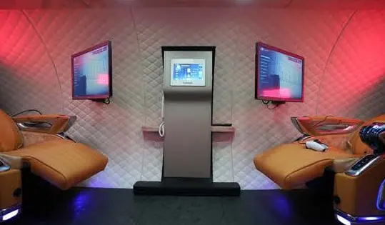 Two tan recliners facing screens and a control column